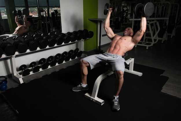 Homme fort dans la salle de gym et exercice de la poitrine avec des haltères Muscular Athletic Bodybuilder Fitness Model Exercise