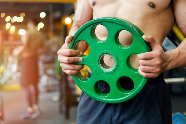 Homme fort exerce dans la salle de gym par des haltères