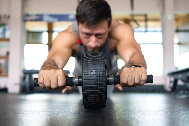 Homme fort faisant des abdominaux à l'aide d'un rouleau dans la salle de sport