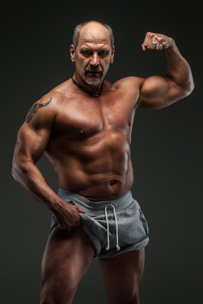 Homme fort et musclé d'âge moyen qui pose en studio. Isolé sur gris.