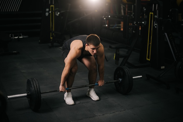 Homme fort musclé avec un beau corps parfait portant des vêtements de sport soulevant des haltères lourdes du sol