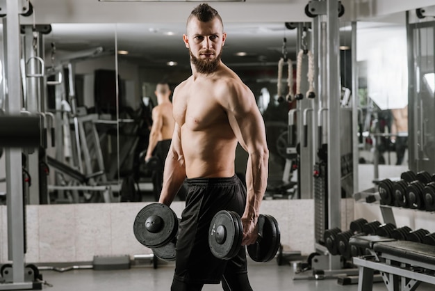 Homme fort musclé faisant des exercices avec des haltères dans la salle de gym