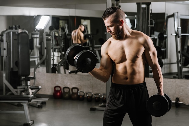 Homme fort musclé faisant des exercices avec des haltères dans la salle de gym