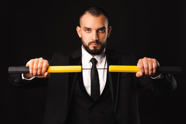 Un homme fort et sérieux portant un costume et une cravate noirs tient un nunchaku