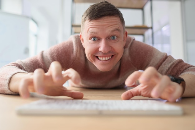 Un homme fou tape sur un clavier blanc avec des doigts regardant à huis clos avec un sourire à pleines dents joyeux