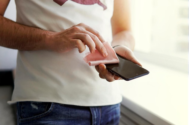 L'homme frotte l'écran de son smartphone noir avec un chiffon. Prévention du coronavirus et des maladies virales. Nettoyer le téléphone portable de la poussière.