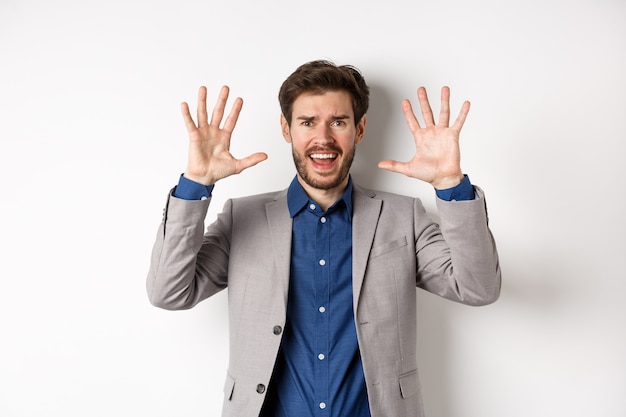 Homme frustré abandonnant, levant les mains pour se rendre et crier, se disputer, porter un costume et à la détresse, fond blanc.