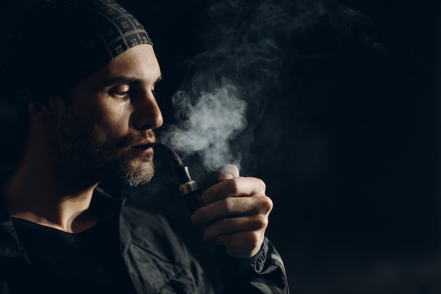 Homme fumant une pipe sur dark. Portrait de profil.