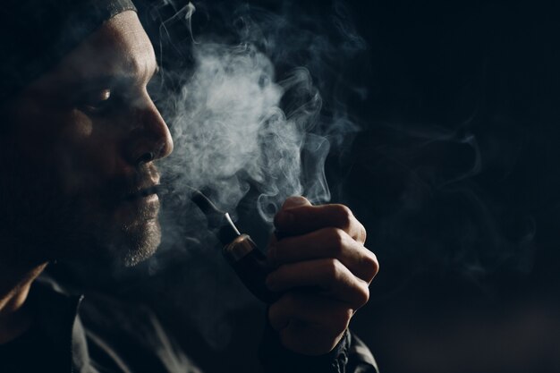 Homme fumant une pipe sur fond sombre. Portrait de profil rétro-éclairé.