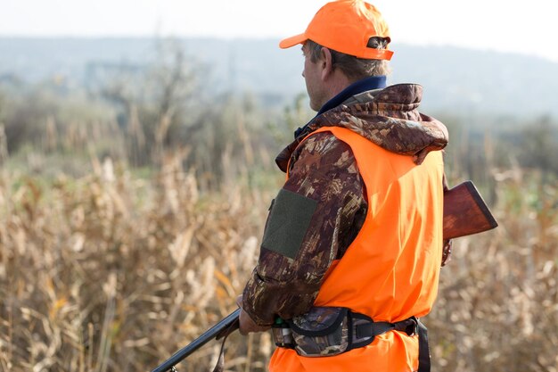 Un homme avec un fusil dans ses mains et un gilet orange sur une chasse au faisan dans une zone boisée par temps nuageux Chasseur avec des chiens à la recherche de gibier