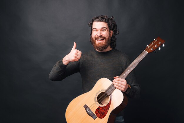 Homme gai avec barbe montrant le pouce vers le haut et tenant la guitare acoustique