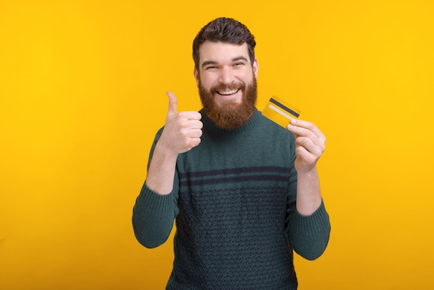 Homme gai avec barbe tenant la carte de crédit et montrant le geste du pouce en l'air