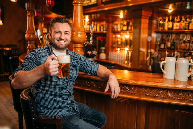 Homme gai avec chope de bière au comptoir de pub. Homme barbu avec verre d'alcool s'amusant au bar