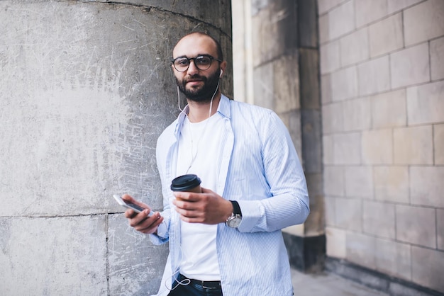 Homme gai dans les écouteurs avec smartphone et café à emporter