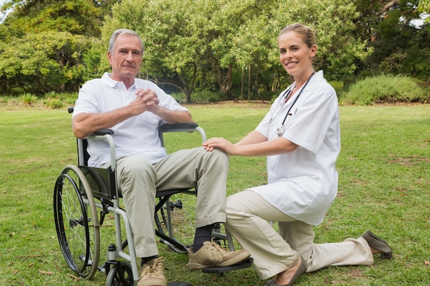 Homme gai dans un fauteuil roulant avec son infirmière agenouillée à côté