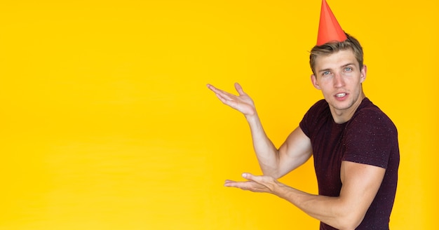 Homme gai sur fond jaune avec une casquette festive sur la tête. pointe avec les mains vers un espace vide pour le texte