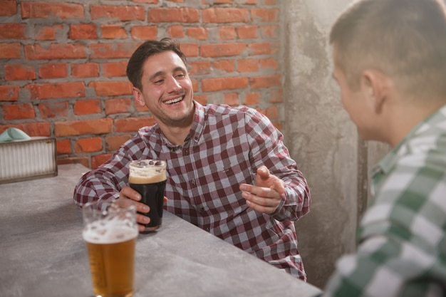 Homme gai riant, parlant à son ami autour d'un verre de bière