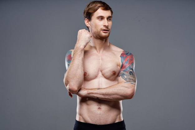 Homme gai avec un tatouage de corps musclé gonflé sur ses bras posant