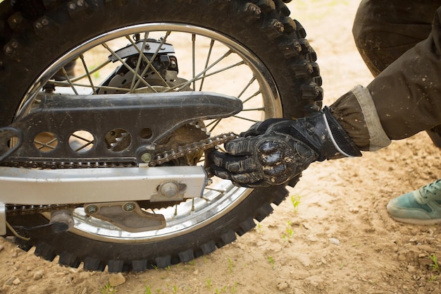 Homme en gants ajustant la chaîne sur la roue arrière de la moto. Cycliste fixant sa conduite en mettant la chaîne sur un pignon. Vue détaillée en gros plan sur certaines parties du véhicule de vélo tout-terrain, réglage de jour.