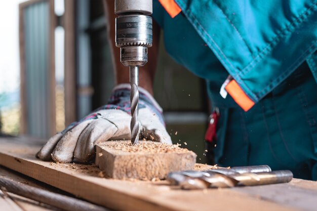 Un homme en gants perçant un gros plan de planche de bois. Travail du bois dans l'atelier