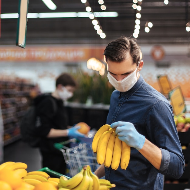Homme en gants de protection choisissant des bananes dans un supermarché