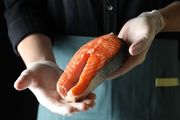 L'homme en gants tient la viande de saumon sur fond sombre