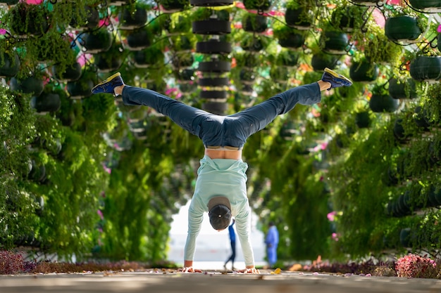 Photo l'homme garde l'équilibre sur les mains dans l'arche florale colorée et parapluie à la station corniche. doha, qatar. concept de santé et de force.