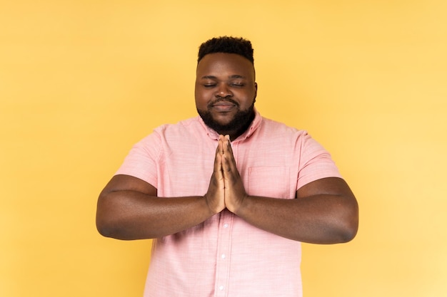 L'homme garde les mains dans le geste de yoga a une expression faciale calme en gardant les paumes pressées ensemble