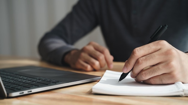 L'homme gaucher écrit dans un cahier sur la table avec un ordinateur portable