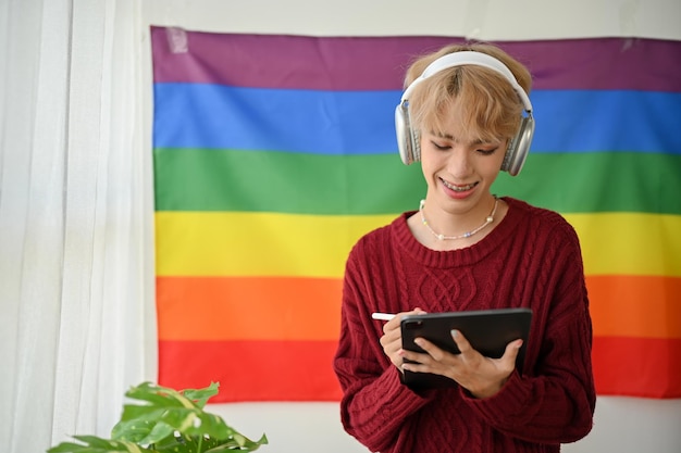 Un homme gay asiatique heureux écoute de la musique et utilise sa tablette tout en se tenant dans sa chambre