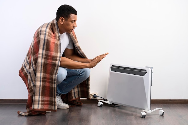 Homme gelé dans des vêtements chauds assis près du radiateur sur fond blanc