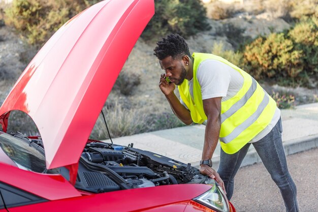 Homme en gilet jaune regardant sous le capot d'une voiture rouge