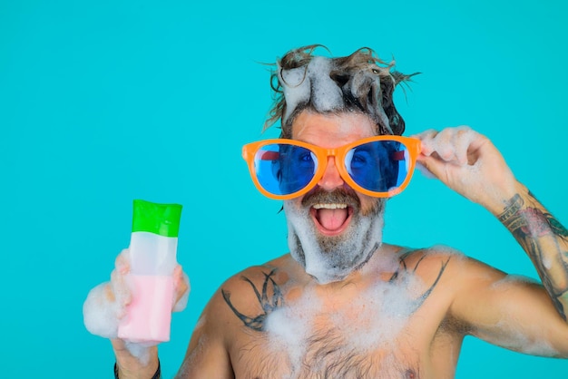 L'homme à grands verres tient la bouteille de shampoing homme dans la douche l'homme avec de la mousse sur la tête la tête de la bouteille de shampoing