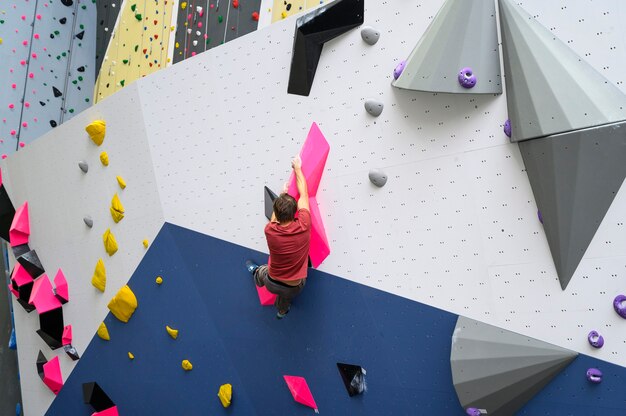 Homme grimpeur sur mur d'escalade artificiel dans une salle de sport de bloc