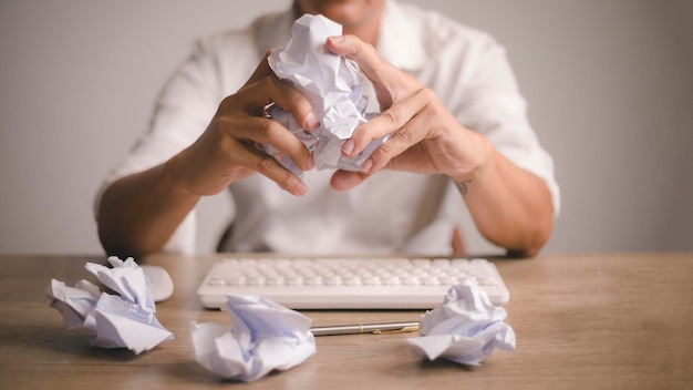 L'homme en gros plan écrase le papier tandis que, avec de nombreuses boules de papier froissées sur le bureau,