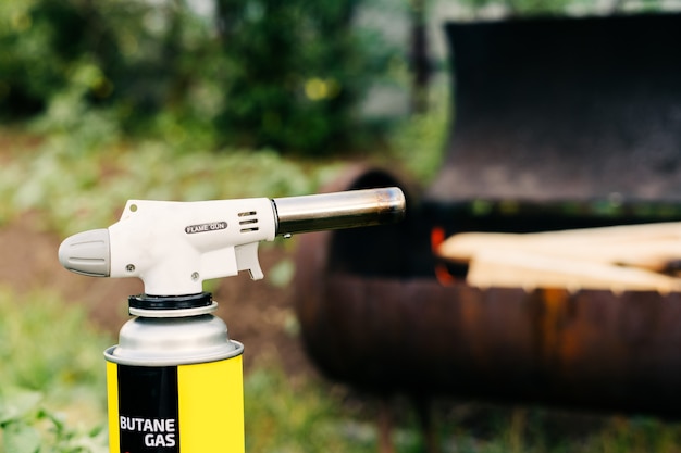 L'homme en gros plan tient un brûleur à gaz avec un ballon et fait un feu dans le pistolet à flamme grill sur le