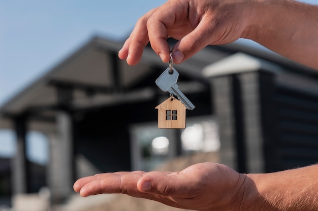 L'homme en gros plan tient les clés de la maison dans ses mains sur fond de bâtiments résidentiels