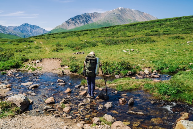 Homme avec gros sac à dos traverse le ruisseau de montagne sur des pierres