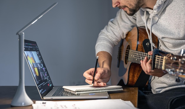 Un homme avec une guitare devant un ordinateur portable à une heure tardive apprend à jouer