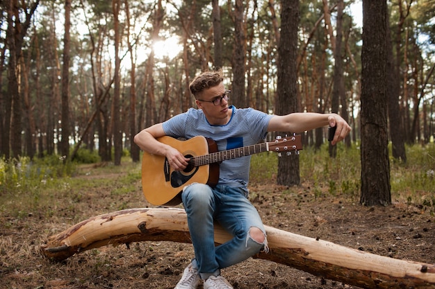 L'homme guitariste fait un selfie au téléphone dans la forêt. Mode de vie de l'artiste.