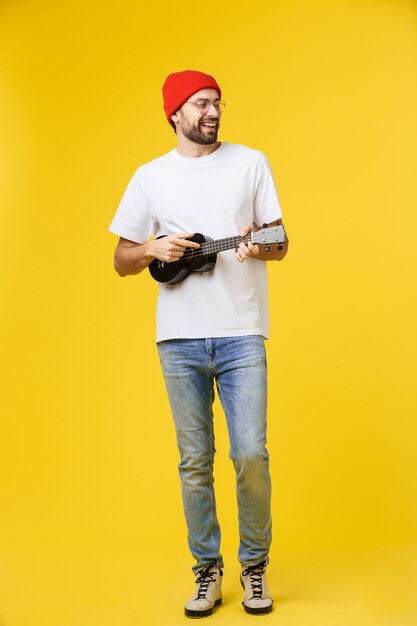 L'homme guitariste joue sur la guitare électrique avec des émotions vives, isolé sur jaune.