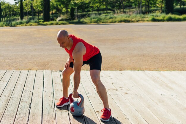 Homme de gymnastique faisant une séance d'entraînement de kettlebell sur une plate-forme en bois.