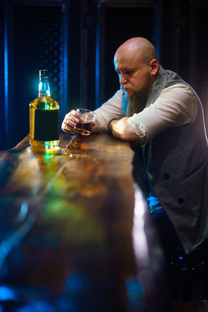 Un homme habillé en décontracté est assis au bar et boit de l'alcool dans un verre