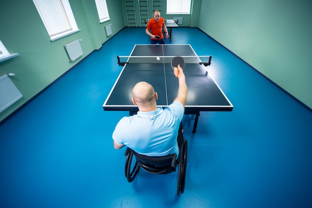 Homme handicapé adulte dans un fauteuil roulant jouer au tennis de table avec son entraîneur