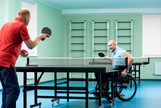 Homme handicapé adulte dans un fauteuil roulant jouer au tennis de table avec son entraîneur