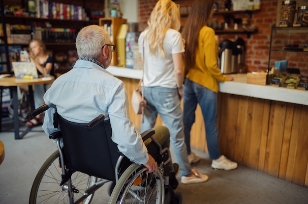 Homme handicapé adulte en fauteuil roulant dans une file d'attente dans un café, handicap, intérieur de la cafétéria sur fond. Homme âgé handicapé, personnes paralysées dans les lieux publics