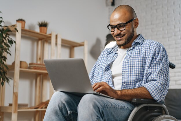 Homme handicapé assis dans un fauteuil roulant et utilisant un ordinateur portable