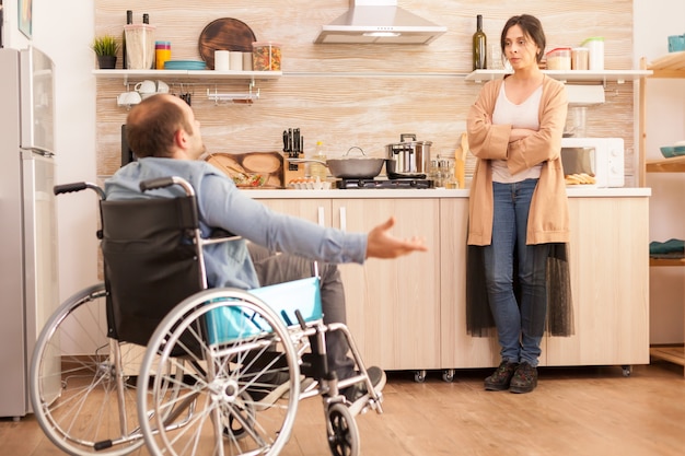 Homme handicapé en fauteuil roulant ayant un différend avec sa femme dans la cuisine. Homme handicapé paralysé handicapé avec incapacité à marcher s'intégrant après un accident.