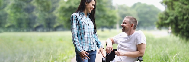 Homme handicapé en fauteuil roulant et femme marchant dans le parc