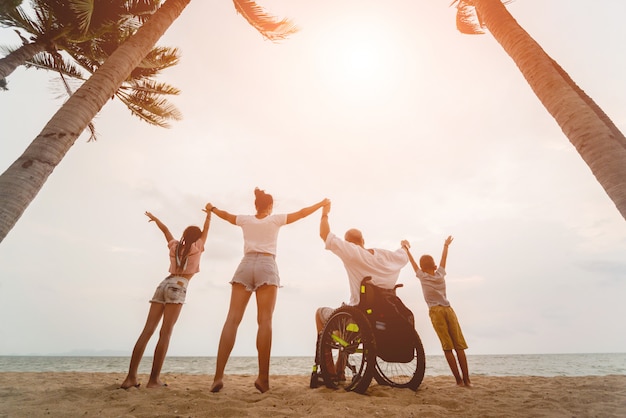 Homme handicapé en fauteuil roulant avec sa famille sur la plage. Silhouettes au coucher du soleil